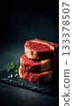 Premium boneless ribeye steaks with heavy marbling, thick cut, displayed in neat stack on black slate board 133378507