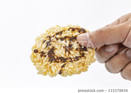Hand Holding a Crispy Rice Snack Drizzled with Dark simmered cane sugar Against a White Background in Close-Up Detail Hand Holding a Crispy Rice Snack Drizzled with Dark simmered cane sugar Against a White Background in Close-Up Detail 133378656