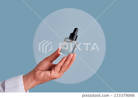 Hand holding serum dropper bottle for skincare routine Hand holding serum dropper bottle for skincare routine 133379066