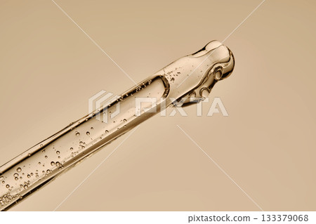 The texture of the serum flowing out of the pipette on a beige background. 133379068