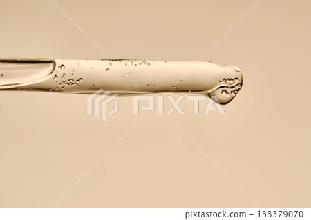The texture of the serum flowing out of the pipette on a beige background. 133379070