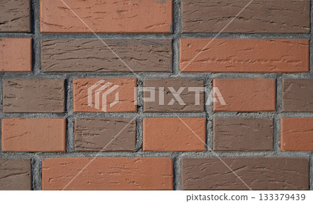 Close up view of brick wall features alternating pattern of red orange and brown bricks. The surface has rough, textured appearance with distinct mortar lines. Background for interior design projects. Close up view of brick wall features alternating pattern of red orange and brown bricks. The surface has rough, textured appearance with distinct mortar lines. Background for interior design projects. 133379439