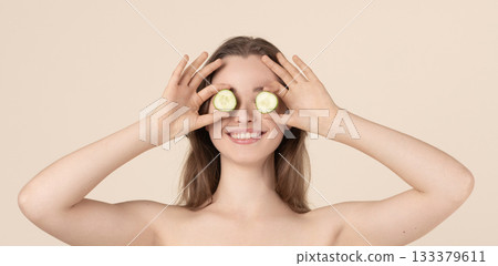 Beautiful young woman covering her eyes with cucumber slices Beautiful young woman covering her eyes with cucumber slices 133379611