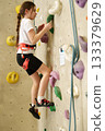 Girl climbing indoor wall in safety harness 133379629