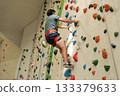 man with safety rope and alpine harness climbing indoor wall with colorful holds 133379633