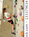 Girl climbing indoor wall in safety harness 133379634