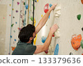 Sporty man climbing with rope and harness on artificial wall in modern fitness center. 133379636