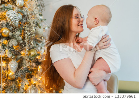 Merry Christmas Xmas. Happy family mother newborn baby child hugging bonding near Christmas tree at home. Mom girl kid celebrating Christmas New Year enjoying winter holidays together. Family moments Merry Christmas Xmas. Happy family mother newborn baby child hugging bonding near Christmas tree at home. Mom girl kid celebrating Christmas New Year enjoying winter holidays together. Family moments 133379661