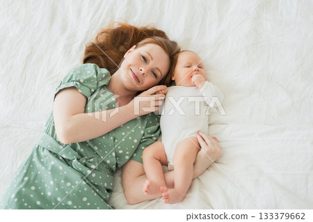 Happy family at home. Mother playing with little toddler child on bed. Mom baby relax playing having fun together. Mother looks at camera with love care. Mom of breast feeding baby rest in living room Happy family at home. Mother playing with little toddler child on bed. Mom baby relax playing having fun together. Mother looks at camera with love care. Mom of breast feeding baby rest in living room 133379662