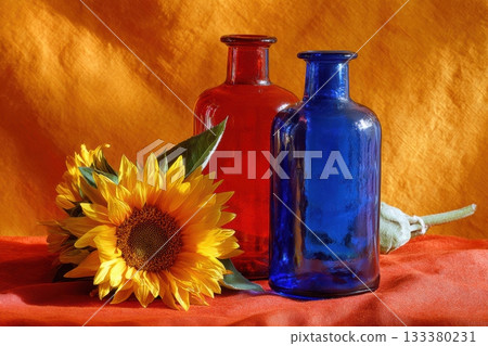 Bright colored bottles and sunflower arranged on fabric Bright colored bottles and sunflower arranged on fabric 133380231
