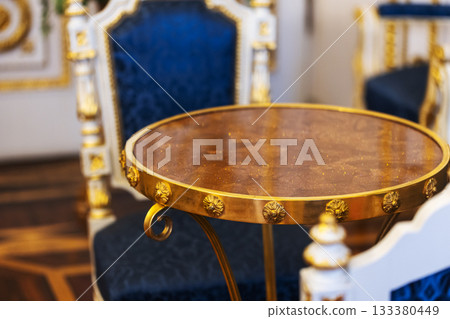 An opulent round table in warm gold with a decorative rim sits in a room 133380449