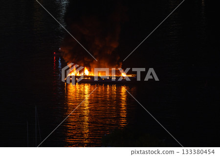 Boat burns on dark water at night, orange flames at night Boat burns on dark water at night, orange flames at night 133380454