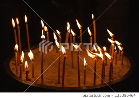 Sacred church scene featuring a round sand tray, several lit prayer candles Sacred church scene featuring a round sand tray, several lit prayer candles 133380464