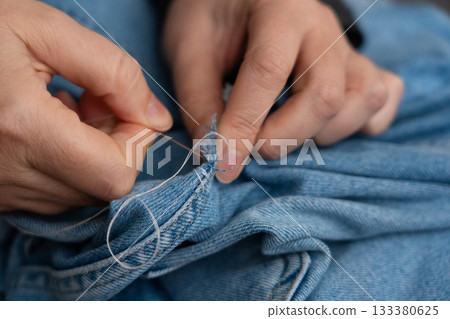 Woman mends jeans by hand with needle Woman mends jeans by hand with needle 133380625