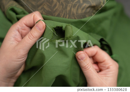 Woman darning a green jacket by hand with needle and patch fabric 133380628