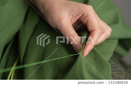 Woman darning a green jacket by hand with needle and patch fabric Woman darning a green jacket by hand with needle and patch fabric 133380630