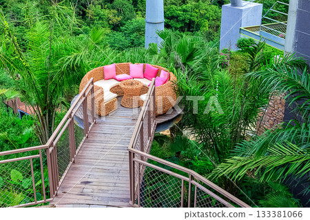 A circular rattan seating area with pink cushions against a backdrop of lush tropical plants in Yanoda Park, Sanya, Hainan, China 133381066