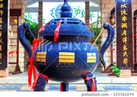A large bronze vessel with red ribbons and gold patterns stands in front of the temple. 133381074