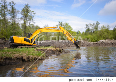 Excavator near small river or pond in countryside. Cleaning river from garbage Excavator near small river or pond in countryside. Cleaning river from garbage 133381197