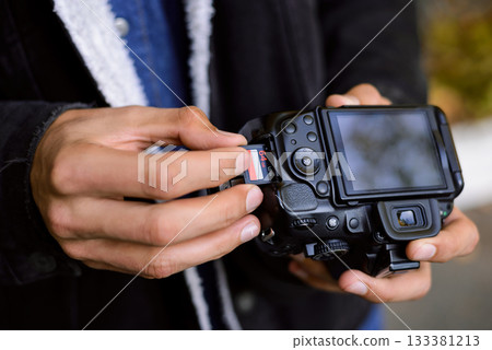 Photographer hand holds Memory card - Flash card near professional DSLR camera. Male photographer ready to insert memory card to his photo camera 133381213
