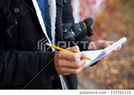 Professional photographer making notes preparing for photoshoot. Young photographer shooting autumn landscapes, choosing the best time to shoot, writing some setting to his notebook Professional photographer making notes preparing for photoshoot. Young photographer shooting autumn landscapes, choosing the best time to shoot, writing some setting to his notebook 133381218