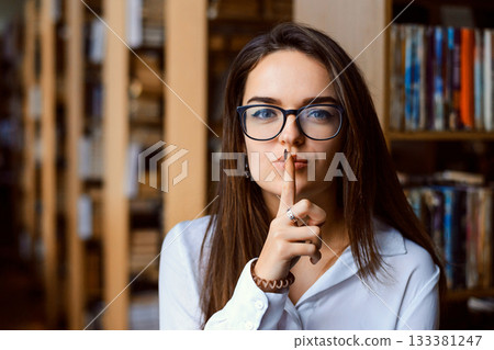 Student woman making silence gesture in a library, preventing from making loud noise in the reading room 133381247