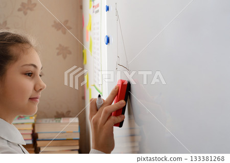 Smiling learner of secondary school doing math geometry task on white markerboard, doing some changes with eraser 133381268