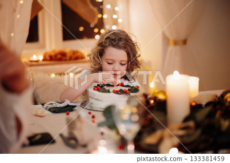 Cheerful small girl looking at christmas cake during christmas dinner. Cheerful small girl looking at christmas cake during christmas dinner. 133381459