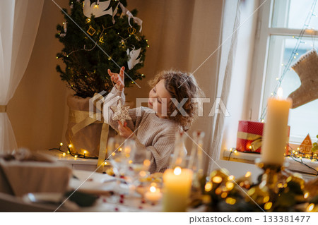 Cheerful small girl indoors at home at Christmas, looking at christmas ornament. Cheerful small girl indoors at home at Christmas, looking at christmas ornament. 133381477