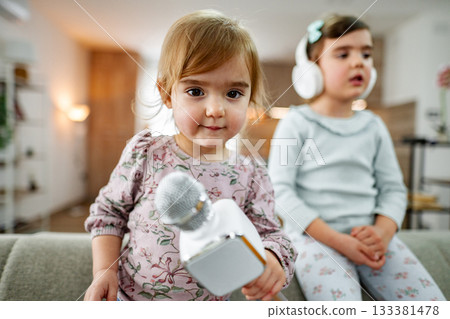 Little girl playing with karaoke microphone at home with her sister Little girl playing with karaoke microphone at home with her sister 133381478