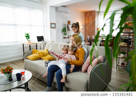 Mother looks at a book and reads a story to her daughters 133381481