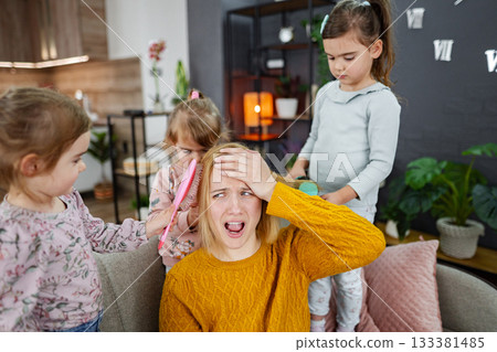 Three little girls are doing their mom's hair 133381485