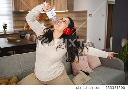 Woman with wireless headphones jumping on sofa and singing at home Woman with wireless headphones jumping on sofa and singing at home 133381500