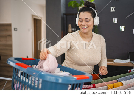 Woman listening to music while hanging the laundry on drying rack at home Woman listening to music while hanging the laundry on drying rack at home 133381506