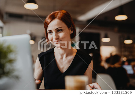 A portrait of woman working remotely from coffee shop, using laptop. 133381509