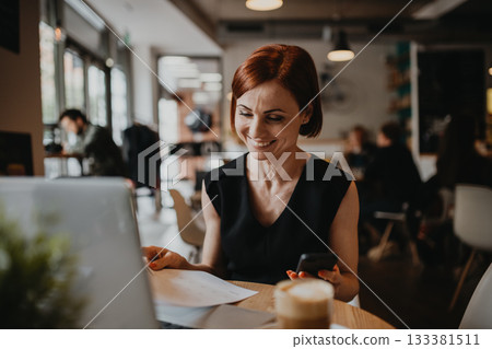A portrait of woman working remotely from coffee shop, using laptop. A portrait of woman working remotely from coffee shop, using laptop. 133381511