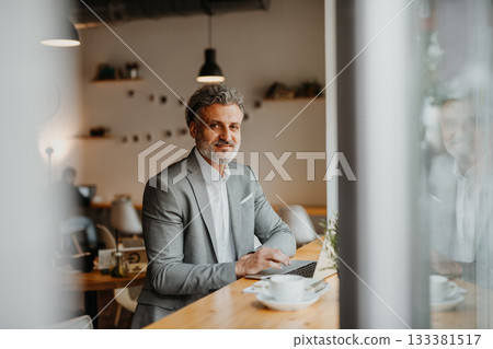 Businessman working remotely from coffee shop, using laptop. Businessman working remotely from coffee shop, using laptop. 133381517