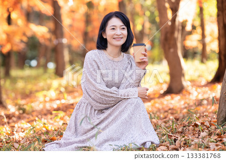A middle-aged woman strolling through a park with autumn leaves 133381768