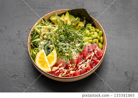 Vibrant tuna poke bowl with rice, avocado, edamame and sesame on dark stone background Vibrant tuna poke bowl with rice, avocado, edamame and sesame on dark stone background 133381865