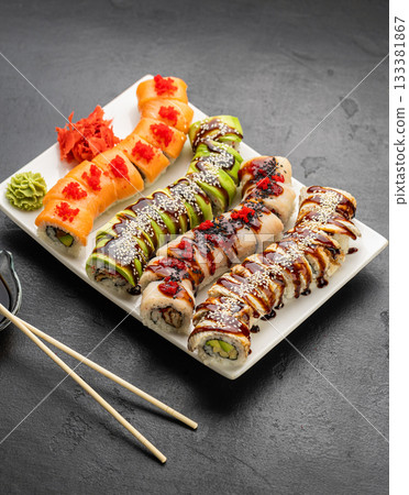 Assorted sushi rolls on platter with soy sauce, wasabi and ginger on black stone Assorted sushi rolls on platter with soy sauce, wasabi and ginger on black stone 133381867