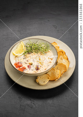 Creamy seafood chowder with lemon and microgreens, served with toasted baguette slices 133381868