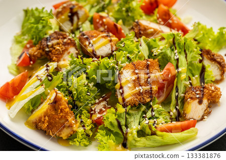 Crispy chicken salad with lettuce, tomatoes, sesame and dressing on plate 133381876