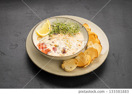 Creamy seafood chowder with lemon and microgreens, served with toasted baguette slices 133381883