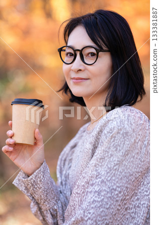 A middle-aged woman strolling through a park with autumn leaves 133381887