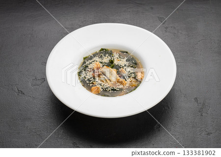Miso soup with salmon, wakame and sesame in white bowl on dark stone table 133381902