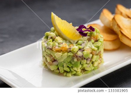Avocado tartare with toasted baguette slices on white plate, gourmet appetizer Avocado tartare with toasted baguette slices on white plate, gourmet appetizer 133381905