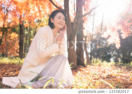 A middle-aged woman strolling through a park with autumn leaves 133382017