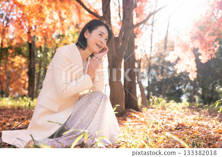 A middle-aged woman strolling through a park with autumn leaves A middle-aged woman strolling through a park with autumn leaves 133382018