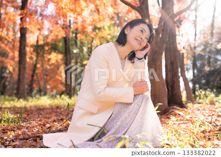 一位中年婦女在秋葉滿布的公園漫步 133382022
