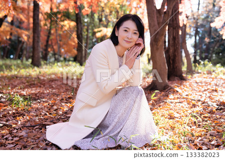一位中年婦女在秋葉滿布的公園漫步 133382023